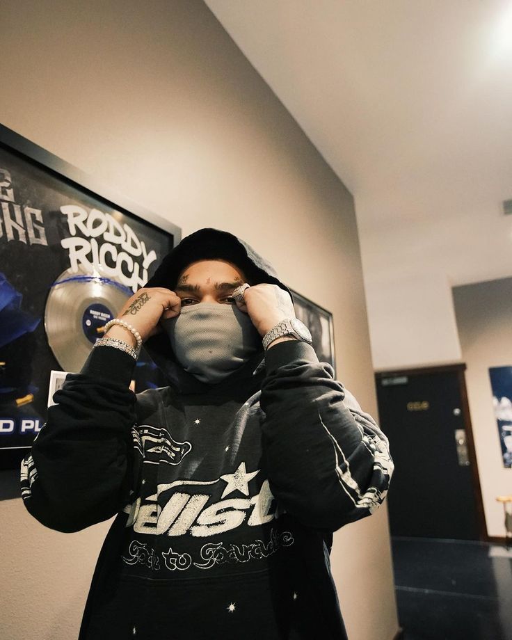 a man in a black jacket is covering his face with a mask while standing in front of a poster