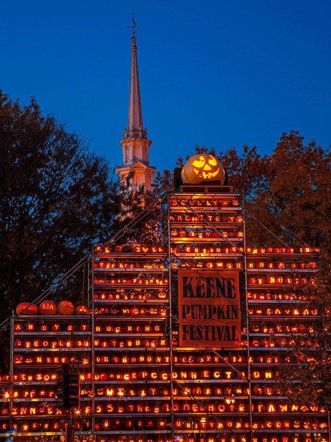 an illuminated building with pumpkins on it and a steeple in the background at night