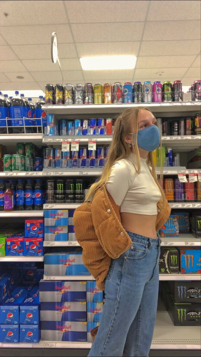 a woman wearing a face mask standing in front of a store shelf filled with cans