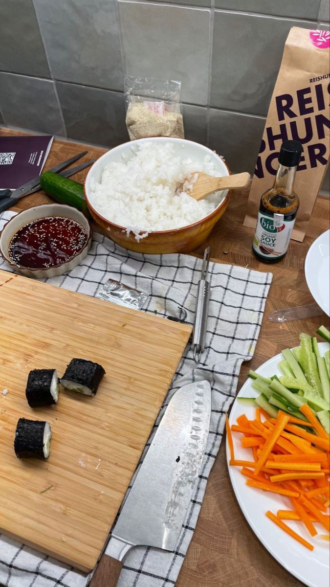 a cutting board topped with sushi and vegetables on top of a wooden table next to a bag of rice