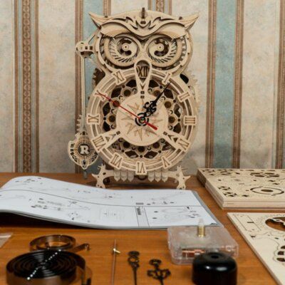 an owl clock sitting on top of a wooden table next to some tools and paper