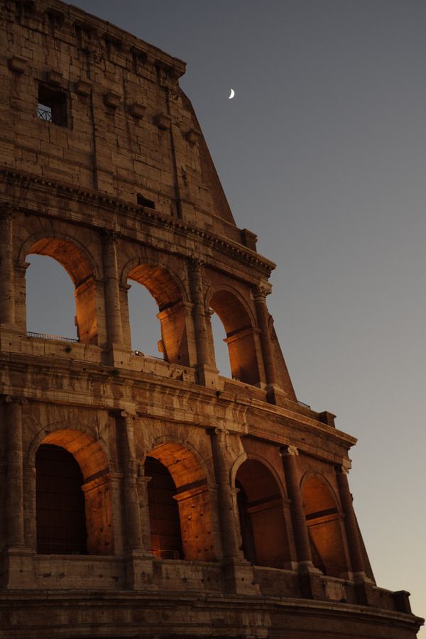 the moon is setting behind an old building with arches and windows on it's side