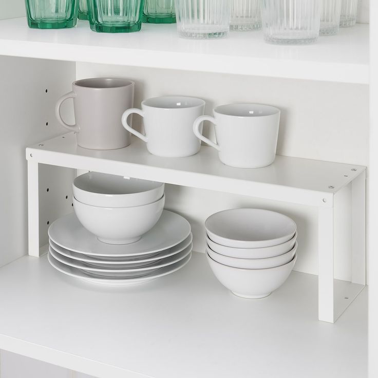 white dishes and cups are stacked on the shelf