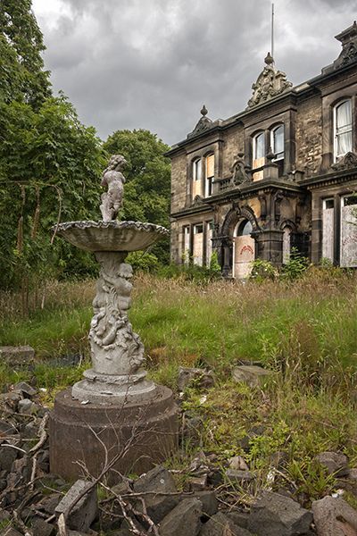 an old abandoned house with a fountain in the foreground and rocks on the ground