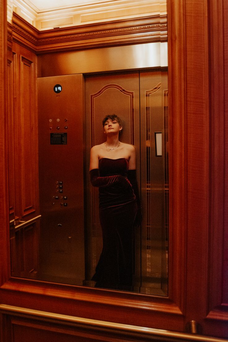 a woman standing in front of a mirror wearing a black dress and holding her head up