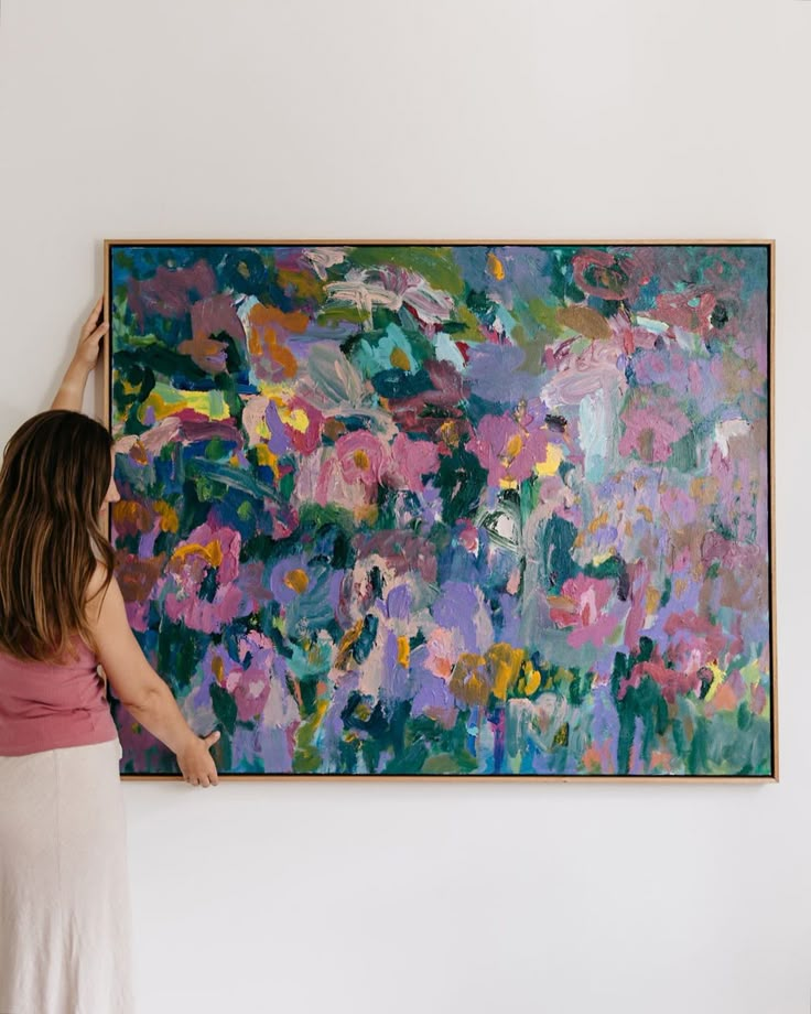 a woman is holding up a large painting on the wall