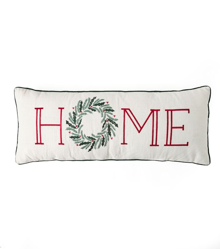 a white pillow with the word home on it and a green wreath in red lettering