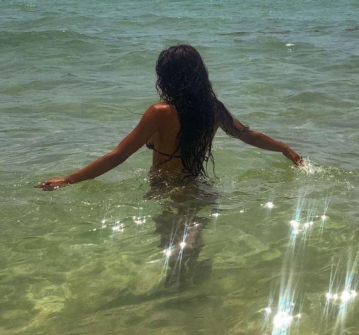 a woman standing in the water with her arms spread out and looking at the ocean