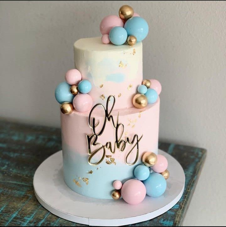 a pink and blue baby shower cake with gold decorations on it's top tier