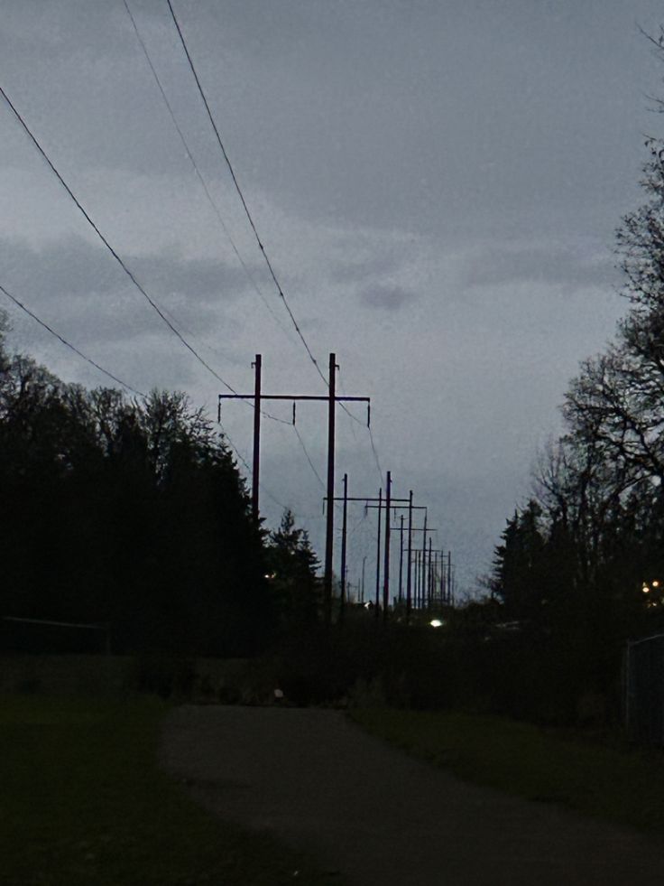 an empty road with power lines and telephone poles in the distance at night, on a cloudy day