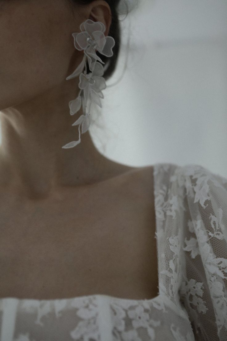 a woman wearing large white earrings with flowers on them