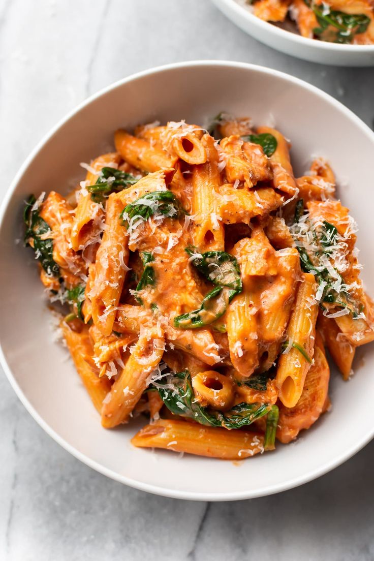 two bowls filled with pasta and spinach on top of a marble countertop,