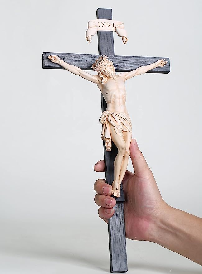 a hand holding a wooden crucifix in front of a white background