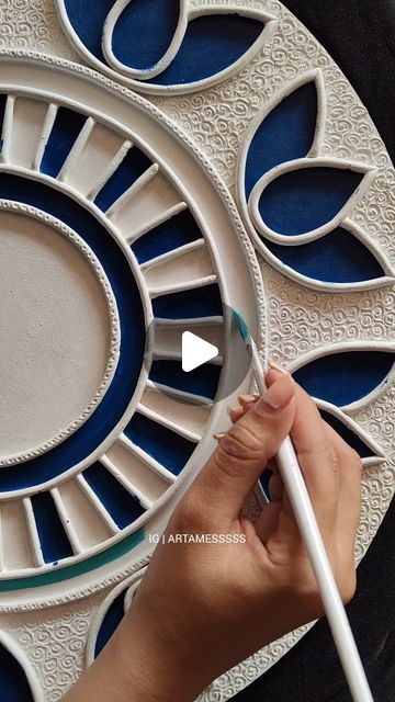 a person holding a paintbrush in front of a circular wall decoration with blue and white designs