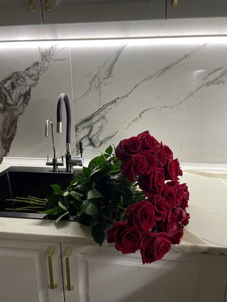 a bunch of red roses sitting on top of a kitchen counter next to a sink