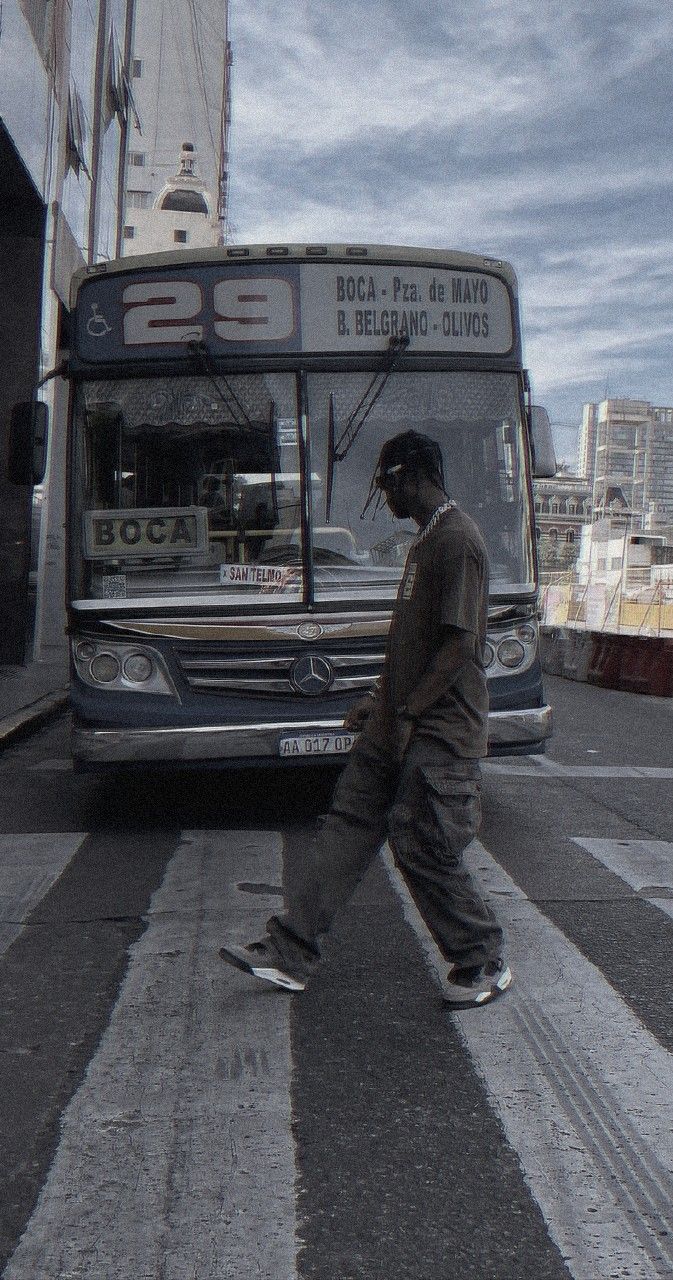 a man walking across the street in front of a bus