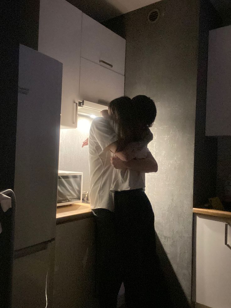 a man and woman hug in the kitchen at night