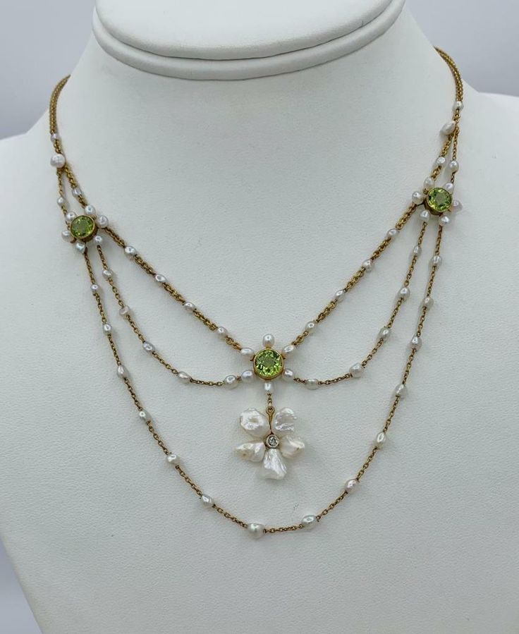 THIS IS A STUNNING VICTORIAN - ART NOUVEAU - BELLE EPOQUE FESTOON NECKLACE WITH THE MOST GORGEOUS NATURAL ROUND FACETED PERIDOT GEMS SET WITH PEARLS AND AN OLD MINE DIAMOND IN A GORGEOUS FLOWER MOTIF FESTOON SWAG DESIGN IN 14 KARAT GOLD. THE NECKLACE DATING TO CIRCA 1900. This is one of the most beautiful festoon necklaces we have seen. The extraordinary Peridot gems are a sparkling green. They are surrounded by a halo of pearls. In the center hangs a beautiful flower with an Old Mine Cut Diamond center and Baroque Pearl petals. The necklace is further adorned with the pearls that are set along the gold chains. The festoon necklace drapes beautifully around the neck. The design is full of the delicate romance of the age and is so special with the flower motifs, the green peridot gems and t Victorian Inspired Jewelry, Pearl Gold Necklace Designs, 18th Century Jewelry Necklaces, Michael Michaud Necklace, Art Nouveau Accessories, Vintage Bead Necklace, Art Nouveau Necklace, Vintage Beaded Necklace, 1890s Jewelry