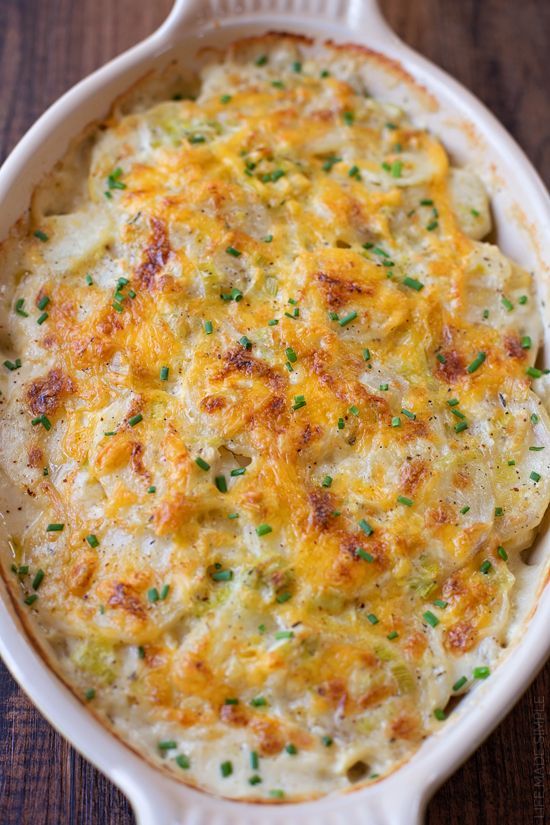 a casserole dish with cheese and green onions in it on a wooden table