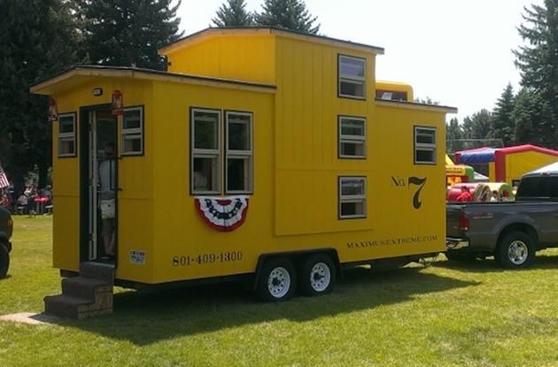 a yellow tiny house on wheels parked in the grass next to a truck and tent