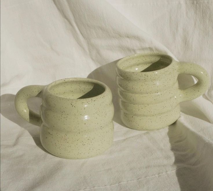 two ceramic mugs sitting on top of a white sheet