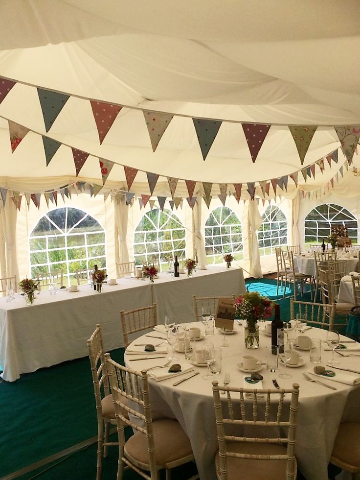 tables and chairs are set up in a tent for an event with bunting on the ceiling