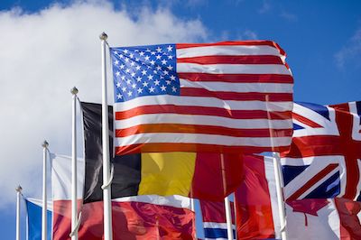 many different flags are flying in the wind on a sunny day with blue sky and white clouds