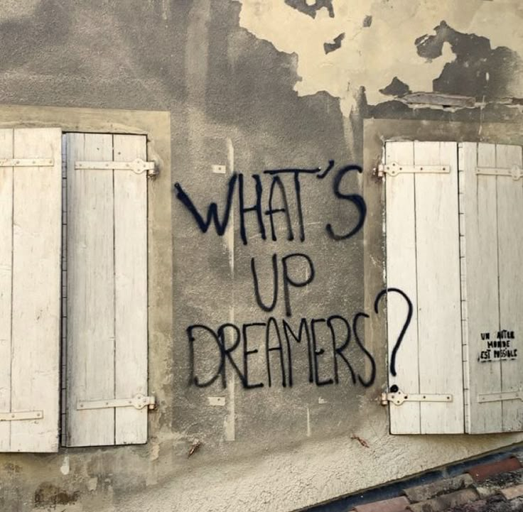 graffiti on the side of an old building with shutters and windows that say what's up dreamers?