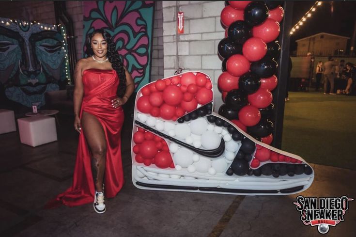 a woman in a red dress standing next to a giant nike shoe with balloons on it