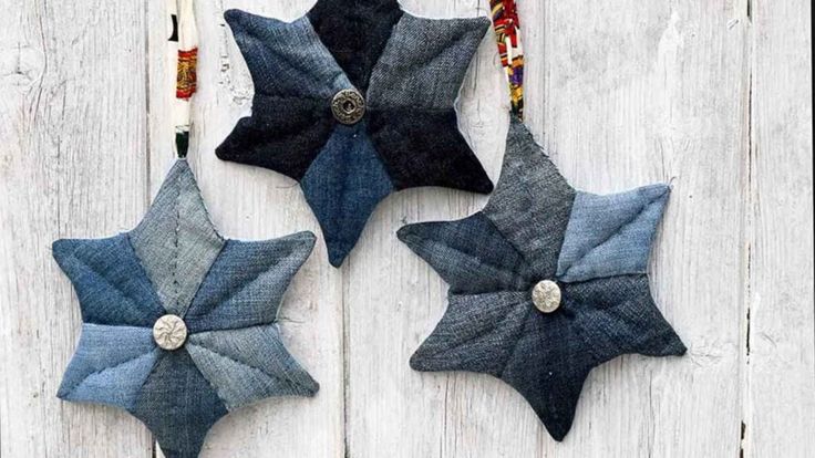 three blue and black stars hanging on a white wooden wall with beaded pins attached to them