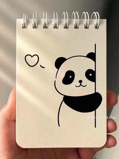 a hand holding a notebook with a drawing of a panda bear on it's cover