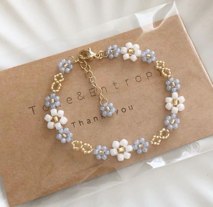 a bracelet with blue and white flowers is shown on top of a brown card that says thank you