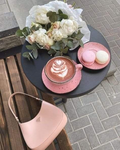 a cup of cappuccino on a table next to a vase with flowers