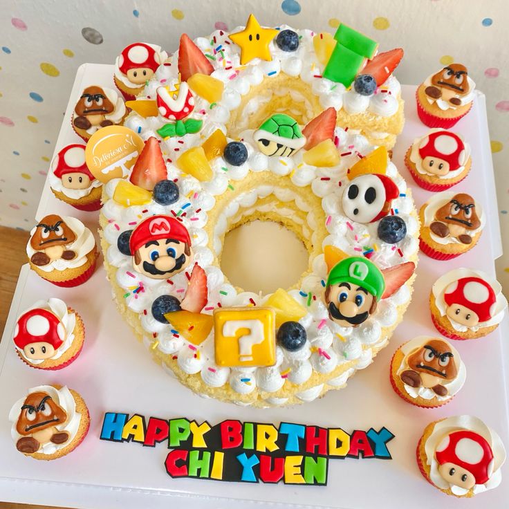 a birthday cake with cupcakes and mario's faces on it, surrounded by other decorations