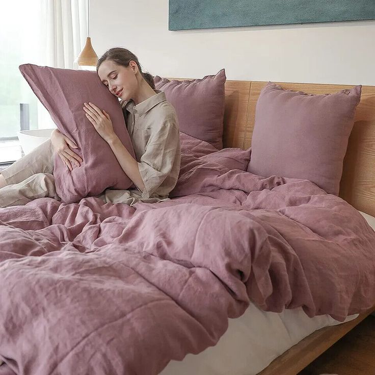 a woman is laying in bed with her arms around the pillow while reading a book