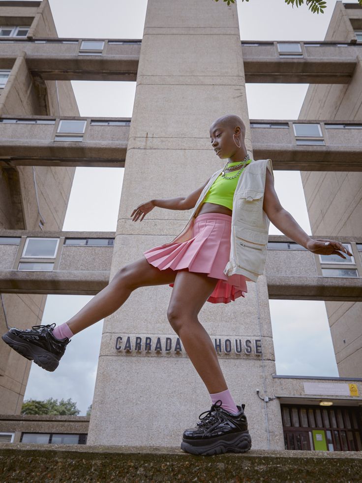 a woman in pink skirt and green shirt standing on the side of a tall building