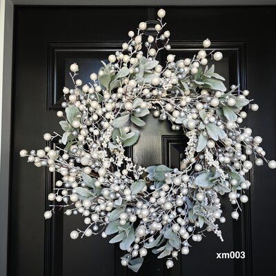 a wreath with white berries and green leaves on a black front door, ready to be decorated for christmas