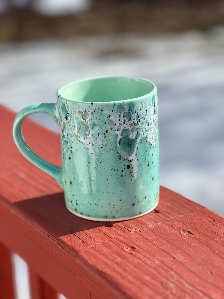 a green mug sitting on top of a red wooden bench next to snow covered ground