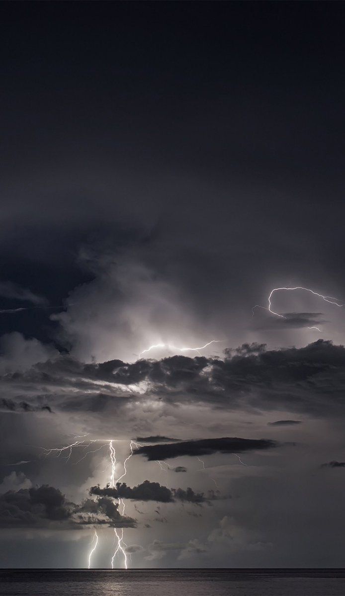 lightning striking over the ocean on a cloudy day