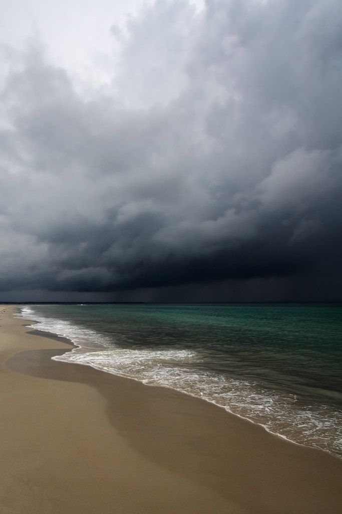 an ocean beach with waves coming in to the shore and dark clouds overhead over it