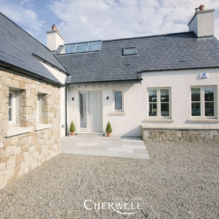 a house with stone walls and windows on the front of it, surrounded by gravel