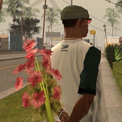 a man holding flowers in his hand on the side of the road with palm trees behind him