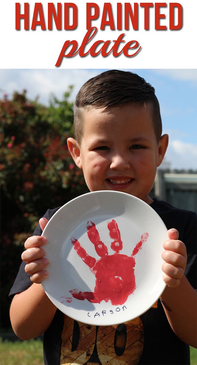 a young boy holding up a paper plate with the words hand painted plate on it