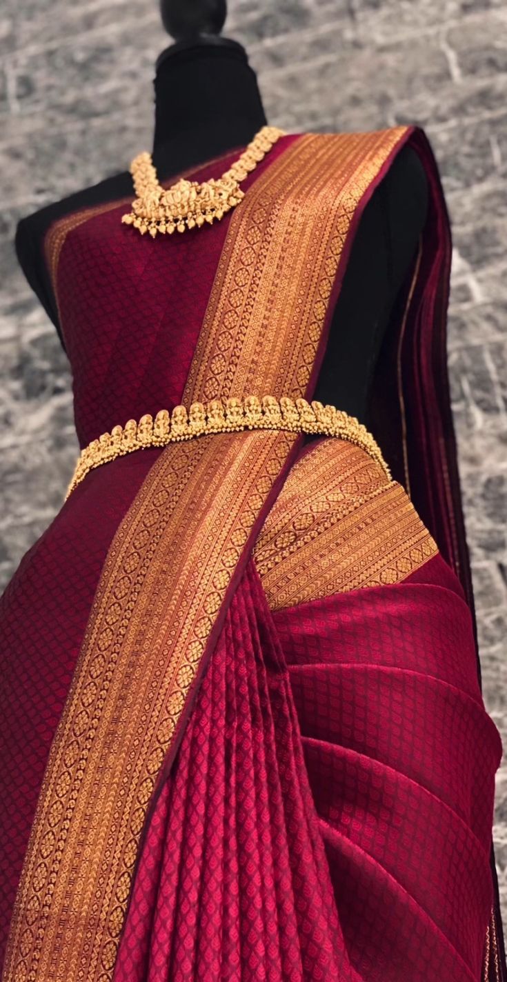 a red and gold colored saree on display in front of a mannequin