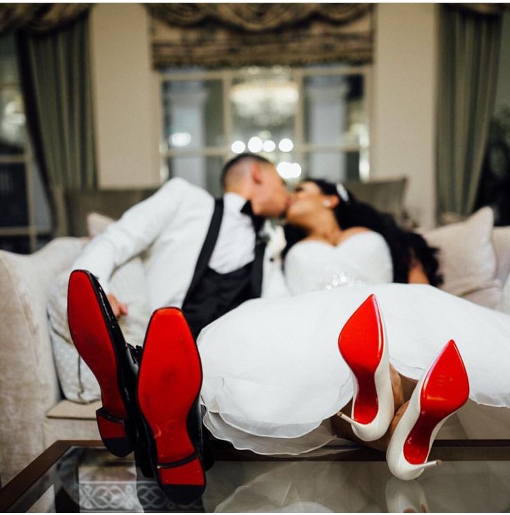 a bride and groom kissing on the couch with red high heeled shoes in front of them