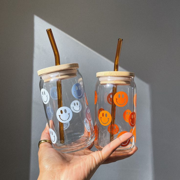 two clear cups with orange and white smiley faces on them, one is holding a straw