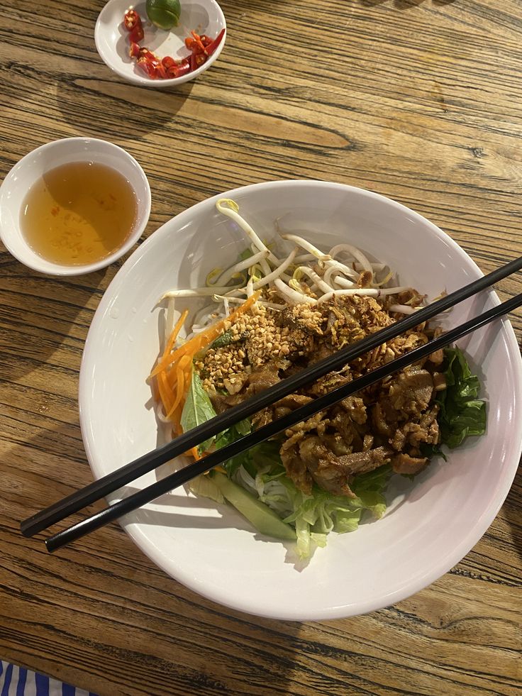 a white plate topped with meat and veggies next to chopsticks on a wooden table