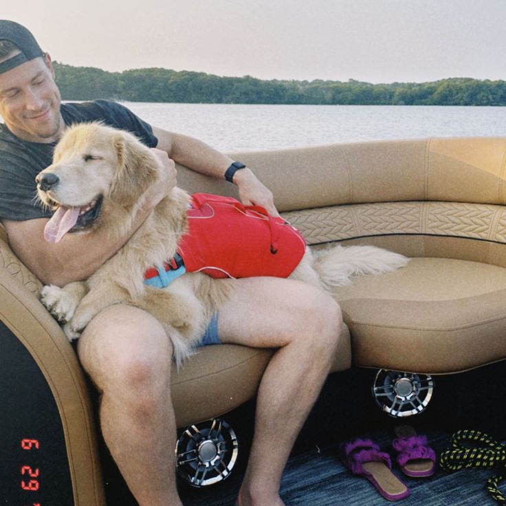 a man sitting on top of a boat with a dog wearing a lifejacket