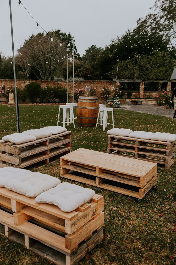 several wooden pallets with pillows on them sitting in the grass next to some chairs