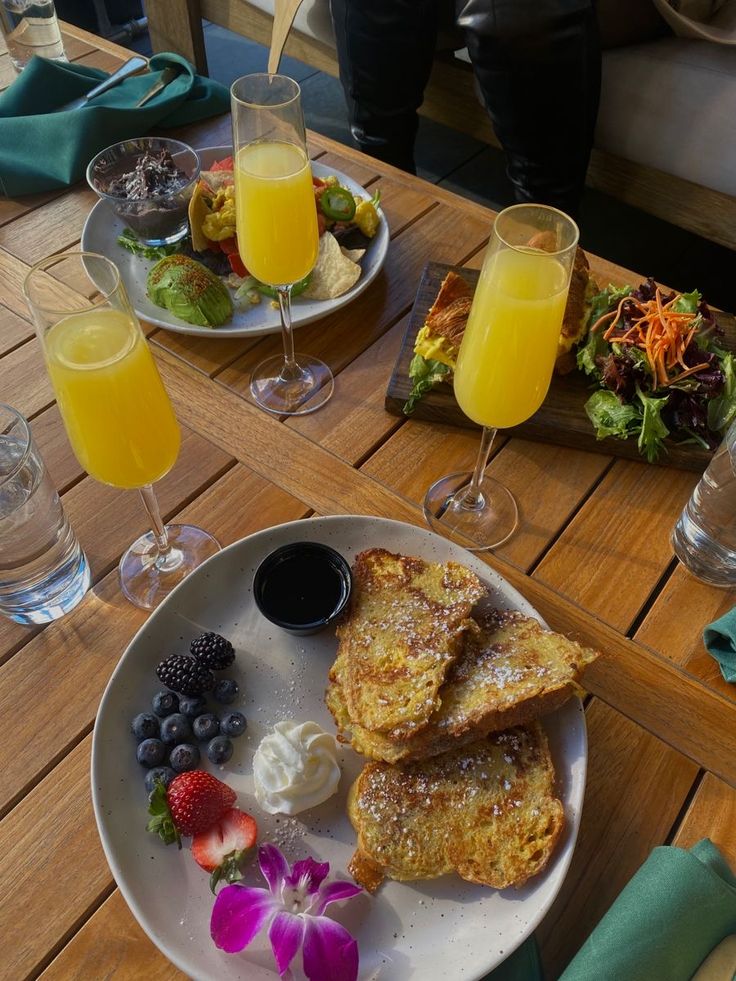 a plate with french toast, fruit, and juice on it sitting on a wooden table